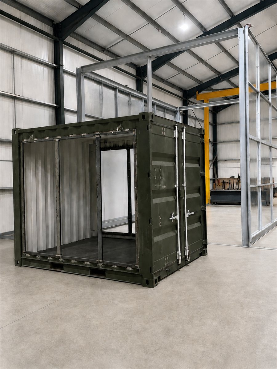 A standard steel shipping container being converted at the Fabrico workshop — one side cut out and reframed to a custom design