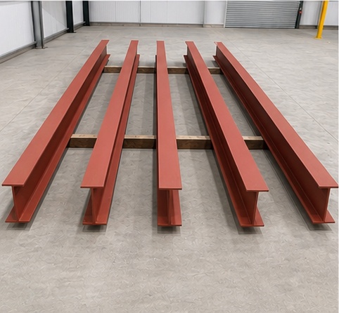 Red-oxide primed structural steel beams laid out on the workshop floor